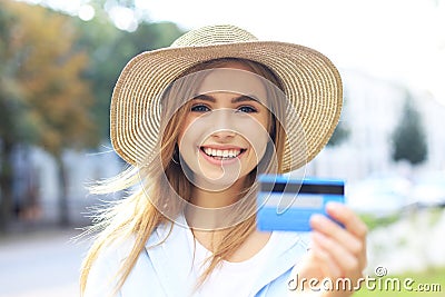 Cheerful young optimistic girl standing outdoors, holding credit card in hand Stock Photo