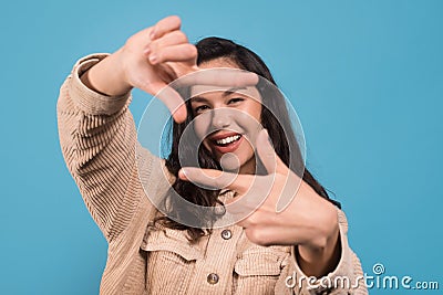 Cheerful young pretty european lady looking through fingers like camera isolated on blue background Stock Photo