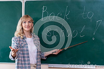 Cheerful young teacher greets students while standing near the blackboard Stock Photo