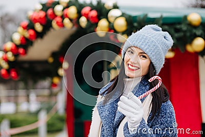 Cheerful young woman holding candy near the street Christmas deciration Stock Photo