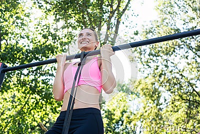 Cheerful young woman wearing pink sports bra while doing chin-up Stock Photo