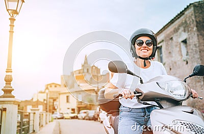 Cheerfully smiling woman in helmet and sunglasses fast riding the moto scooter on the Sicilian old town streets in the Forza d` Stock Photo