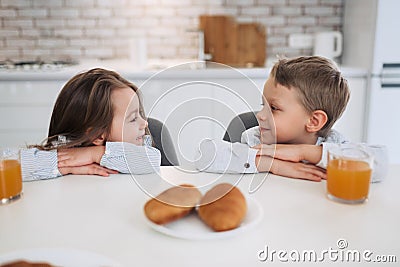 Cheerfulness. Pretty inspired little dark-haired girl smiling and looking at her brother while they having breakfast Stock Photo