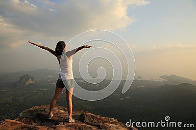 Cheering woman hiker open arms at mountain peak Stock Photo