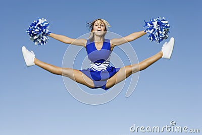 Cheerleader With Pompoms Doing Splits Against Sky Stock Photo