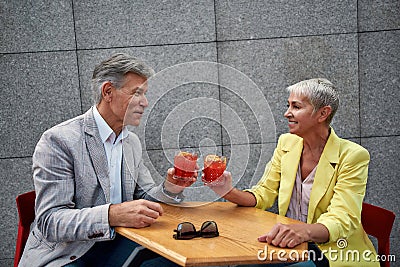 Cheers. Beautiful mature couple in stylish wear drinking cocktails while sitting in cafe outdoors together Stock Photo