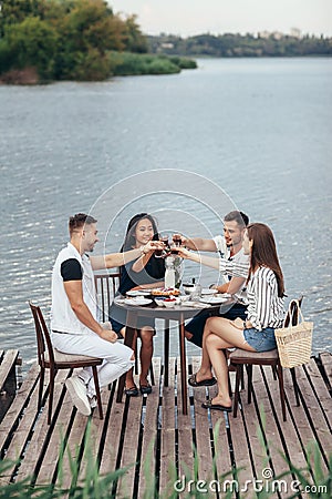 Cheers! Group of friends enjoying outdoor picnic in river pier Stock Photo