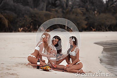 Cheers! Outdoor photo of Appealing Three sexy bikini girls drink wine during a picnic on tropical beach at Maldives island. Slim Stock Photo