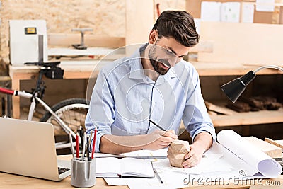 Cheery youthful woodworker doing drawings on example item in workshop Stock Photo