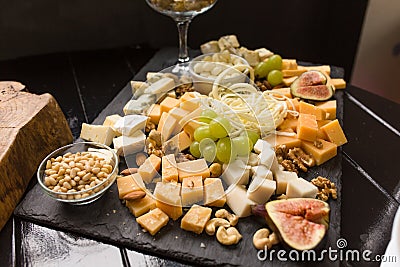 Cheese assorted or cheeseboard. Gourmet cheeses with fig, green grapes and nuts on black wooden plank. Focus on parmesan Stock Photo