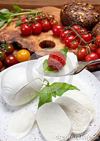 Cheese collection, eating. of white soft Italian cheese mozzarella, served with red cherry tomatoes, fresh basil leaves Stock Photo