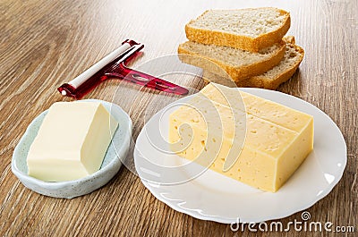 Cheese cutter, slices of bread, butter in plate, piece of cheese in plate on wooden table Stock Photo