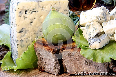 Cheese with mold on a green lettuce leaf with figs on a wooden background. Golden shot glass with alcohol Stock Photo