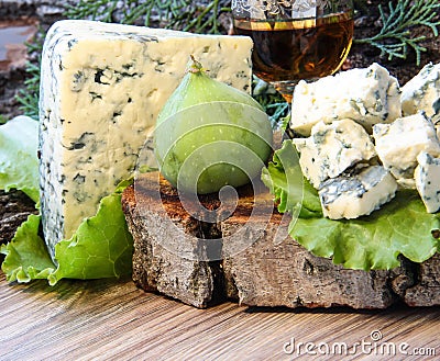 Cheese with mold on a green lettuce leaf with figs on a wooden background. Golden shot glass with alcohol Stock Photo