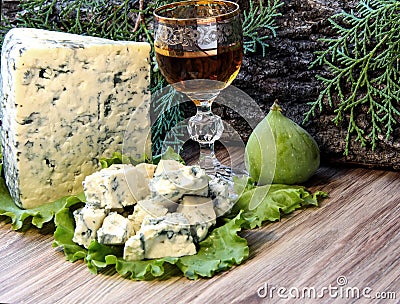 Cheese with mold on a green lettuce leaf with figs on a wooden background. Golden shot glass with alcohol Stock Photo