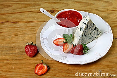 Cheese with a noble blue mold on plate with strawberries and with strawberry sauce, mint, on a wooden background. Top view with co Stock Photo