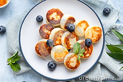 Cheese pancakes, fritters or syrniki with blueberry, physalis and yogurt, blue background. Healthy and tasty breakfast Stock Photo