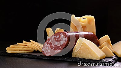 cheese and piece of salami loaf are on black stone board on dark background Stock Photo