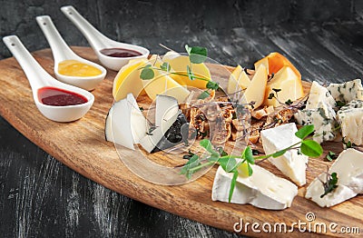 Cheese plate on a dark background. Decorated with fresh herbs and figs. Blurred background. Stock Photo