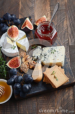Cheese plate with grapes, figs, crackers, honey, plum jelly, thyme and nuts. Stock Photo