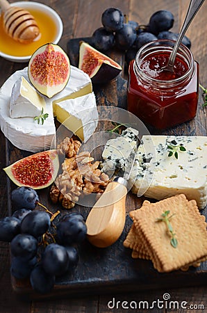 Cheese plate with grapes, figs, crackers, honey, plum jelly, thyme and nuts. Stock Photo