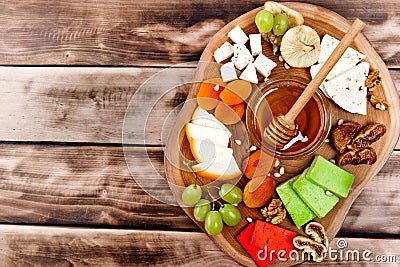 Cheese plate - various types of cheese, honey, grapes, dried apricots, nuts and figs on a wooden board on dark wooden background. Stock Photo