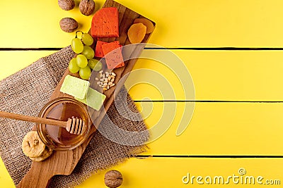Cheese plate - various types of cheese, honey, grapes, dried apricots, nuts and figs on a wooden board on yellow wooden. Stock Photo