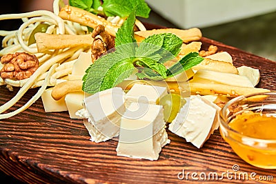 Cheese platter with feta, parmesan, mozzarella, cheese sticks, braid cheese with honey and nuts on the wooden board Stock Photo