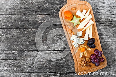 Cheese platter garnished with pear, honey, walnuts, grapes, carambola, physalis on cutting board on wooden background Stock Photo