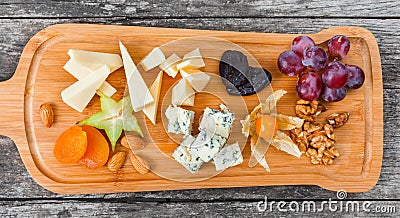 Cheese platter garnished with pear, honey, walnuts, grapes, carambola, physalis on cutting board on wooden background Stock Photo