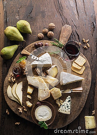 Cheese platter with organic cheeses, fruits, nuts and wine on wooden background. Top view. Tasty cheese starter Stock Photo