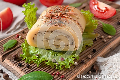 Cheese roll with olive herbs on a lettuce sheet. On a wooden board. Close-up. Decorated with arugula, spices and tomatoes. Stock Photo