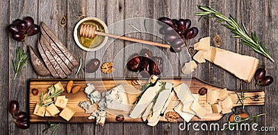 Cheese selection on wooden rustic board. Cheese platter with different cheeses, grapes, nuts, honey and dates on weathered wood b Stock Photo