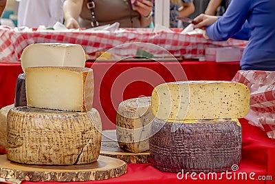 Stacked rounds of cheese are displayed at the outdoor farmers market while people shop Stock Photo