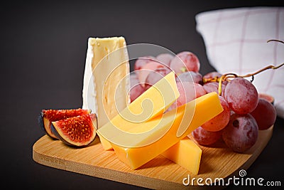 Cheeseboard platter with hard and soft mould cheese, grape and segmented fig on wooden board Stock Photo