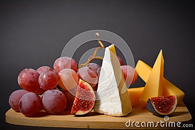 Cheeseboard platter with hard and soft mould cheese, grape and segmented fig on wooden board Stock Photo