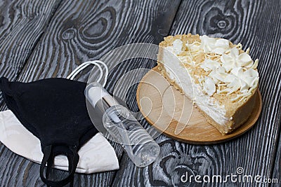 Cheesecake with white chocolate. The filling is visible on the cut. Nearby are medical masks and antiseptic. On pine planks Stock Photo