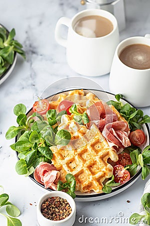 Cheesy belgian waffles served with ham, tomatoes and lettuce corn on white marble background . Savory waffles. Healthy Stock Photo