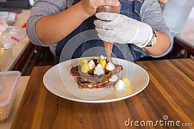 A chef adding cream topping on waffles on a wooden table Stock Photo