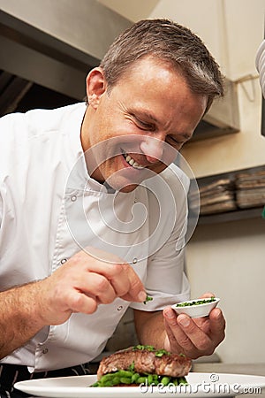 Chef Adding Seasoning To Dish In Kitchen Stock Photo