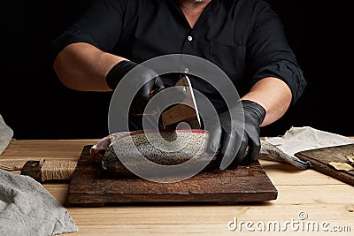 Chef in black shirt and black latex gloves slices a whole fresh fish salmon Stock Photo