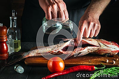 Chef or cook prepares fresh fish bighead carp with add vinegar. Preparation for cooking herring. Working environment in the Stock Photo