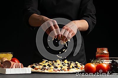 The chef cooks Italian pizza, sprinkles with mozzarella cheese. Freeze in motion. Against the background of pizza ingredients. Stock Photo