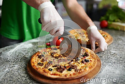 Chef cuts freshly prepared pizza on a wooden substrate. Stock Photo