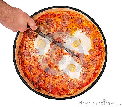 The chef cuts the pizza with a kitchen knife. Pizza with beef sausages, eggs and bacon on the slate plate, isolate on white Stock Photo