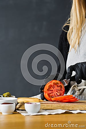 Chef cuts red tomatoes. The concept of cooking a black Burger. Kitchen, side view, space for text. Stock Photo