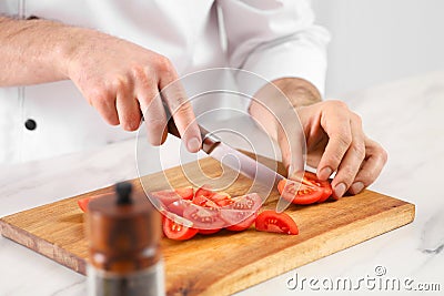 Chef cutting tomatoes at marble table in kitchen, closeup Stock Photo