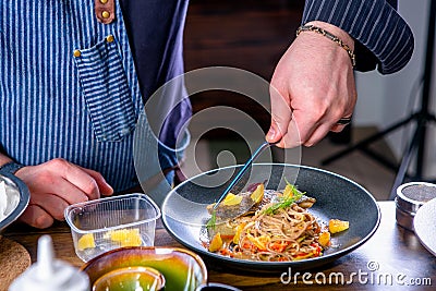 Chef decorates the buckwheat noodles on wok and baked carp. Master class in the kitchen. The process of cooking. Step by step. Stock Photo