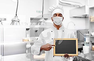 Chef in face mask with chalkboard at kitchen Stock Photo