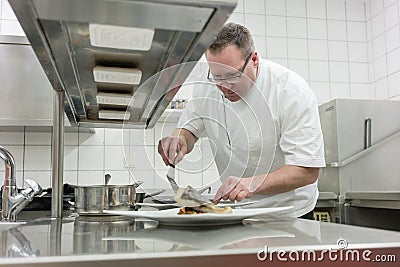 Chef finishing and garnishing fish dish on pass in restaurant kitchen Stock Photo